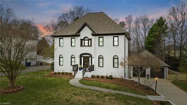 view of front of house with a garage, concrete driveway, a lawn, and roof with shingles