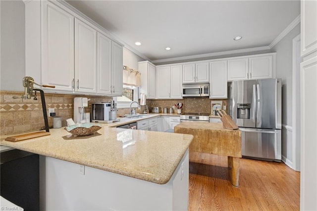 kitchen featuring a peninsula, stainless steel appliances, crown molding, white cabinetry, and a sink