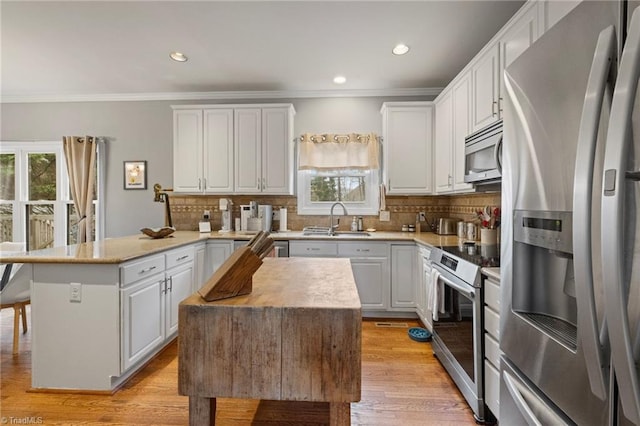 kitchen with stainless steel appliances, tasteful backsplash, light countertops, white cabinetry, and a peninsula