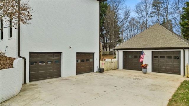 view of side of home featuring a shingled roof, an outdoor structure, and fence