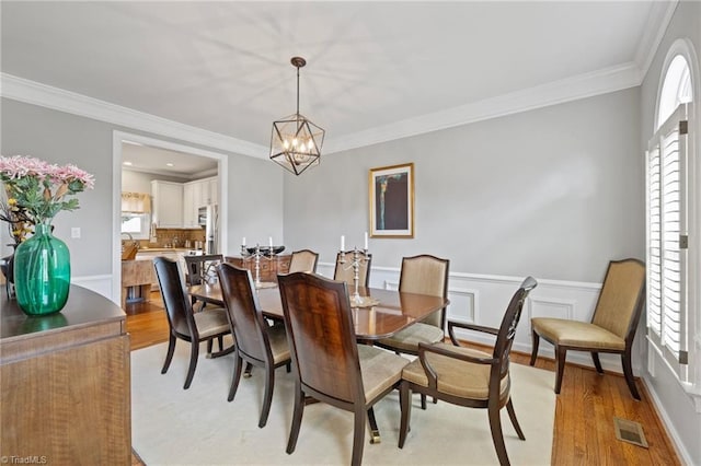 dining room with a chandelier, light wood-type flooring, visible vents, and ornamental molding