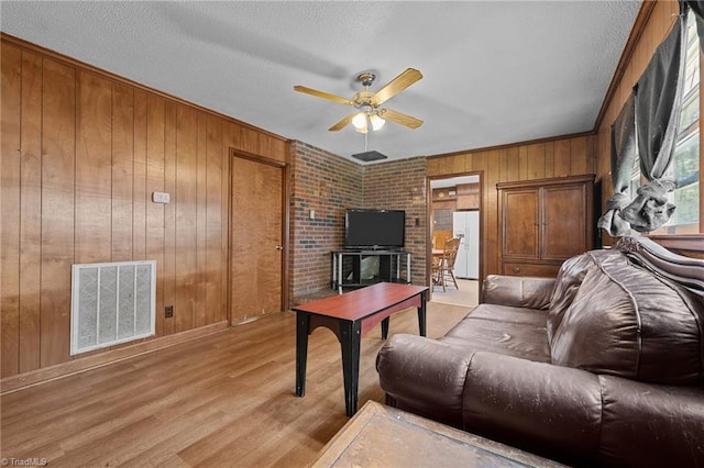 living room with wooden walls, light wood-type flooring, ceiling fan, baseboards, and visible vents