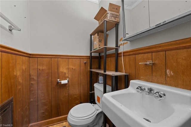 bathroom featuring toilet, a wainscoted wall, a sink, and wooden walls