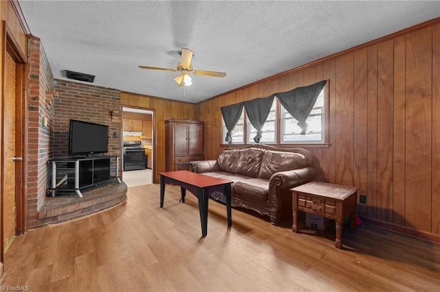 living room featuring ceiling fan, wood walls, light wood-style floors, and a textured ceiling