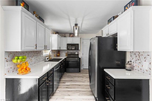 kitchen featuring light wood-style floors, white cabinetry, dark cabinetry, a sink, and stainless steel appliances