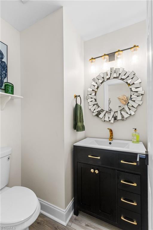 half bathroom featuring baseboards, vanity, toilet, and wood finished floors