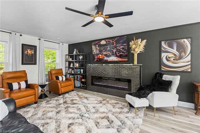 living room with a brick fireplace, ceiling fan, and wood finished floors