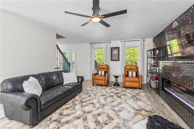living room featuring stairway, a ceiling fan, wood finished floors, and a brick fireplace