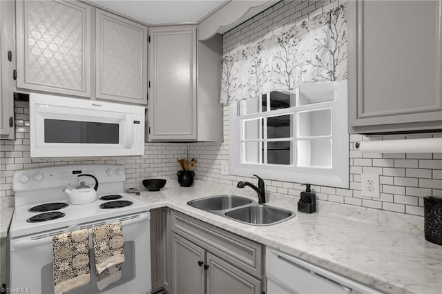 kitchen with sink, light stone counters, white appliances, and decorative backsplash