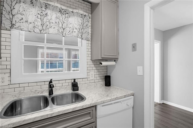 kitchen featuring sink, dark hardwood / wood-style floors, dishwasher, light stone countertops, and backsplash