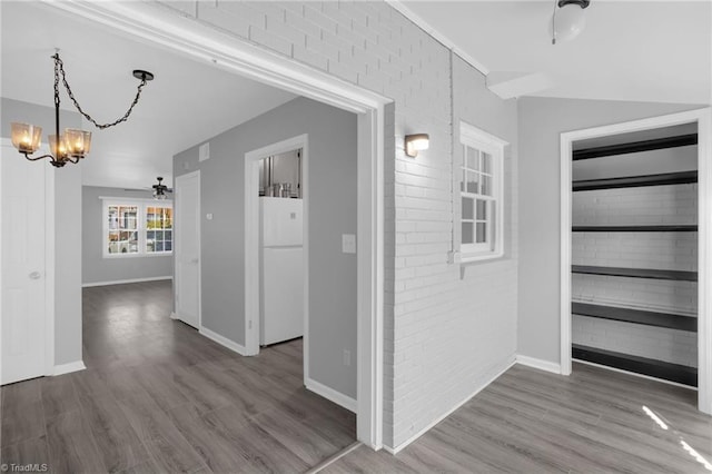 corridor featuring hardwood / wood-style flooring, brick wall, and a chandelier