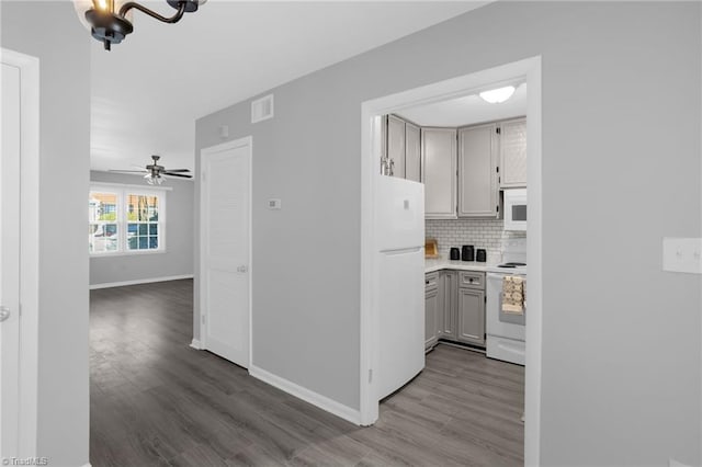 kitchen featuring wood-type flooring, gray cabinets, white appliances, ceiling fan with notable chandelier, and decorative backsplash