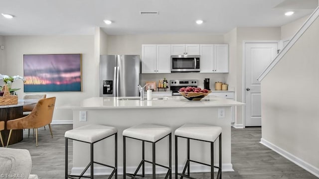 kitchen with visible vents, a kitchen bar, a center island with sink, appliances with stainless steel finishes, and a sink