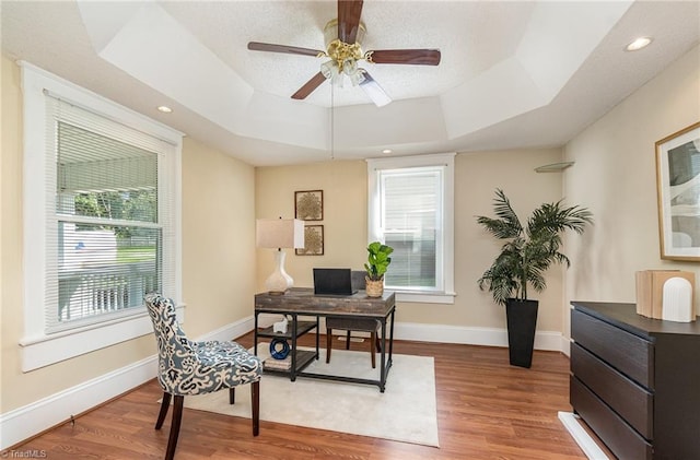 office space featuring wood-type flooring, a raised ceiling, and ceiling fan