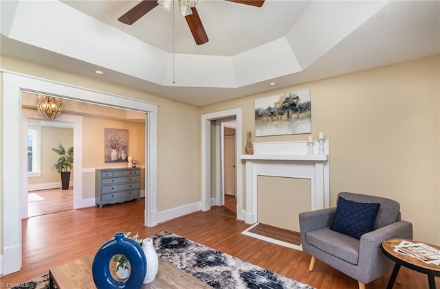 sitting room with ceiling fan, a tray ceiling, and hardwood / wood-style floors