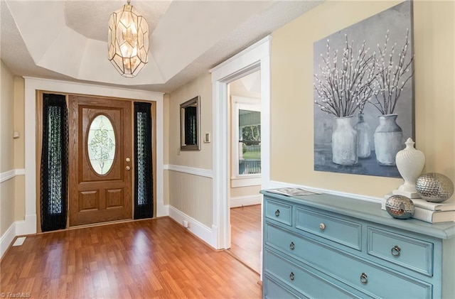 foyer featuring light wood-type flooring, a chandelier, and a raised ceiling