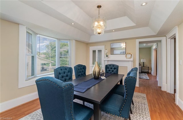 dining space with light hardwood / wood-style floors, a tray ceiling, and a chandelier