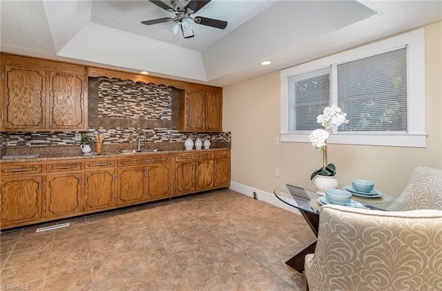 kitchen featuring backsplash, ceiling fan, a raised ceiling, and sink