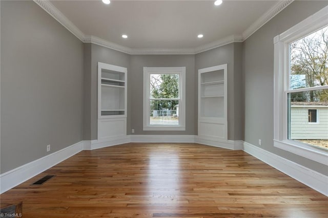 empty room featuring ornamental molding, light hardwood / wood-style flooring, and built in features