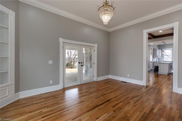 empty room with an inviting chandelier, hardwood / wood-style floors, ornamental molding, built in shelves, and french doors