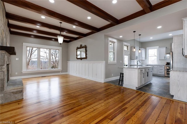 kitchen featuring sink, dark hardwood / wood-style floors, pendant lighting, a kitchen island with sink, and white cabinets