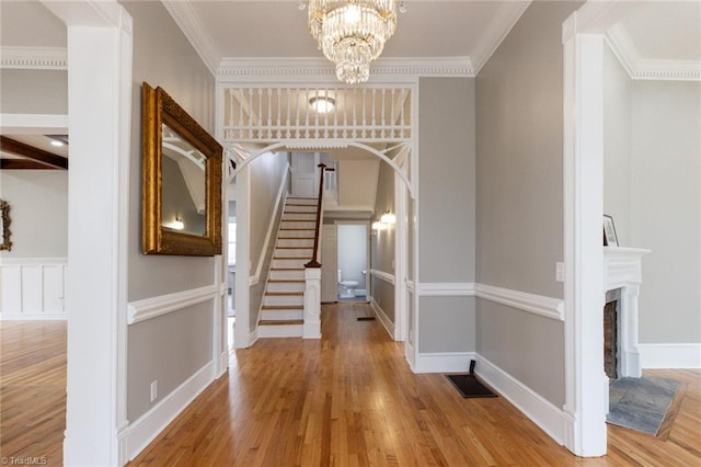 entryway with wood-type flooring, ornamental molding, and a notable chandelier