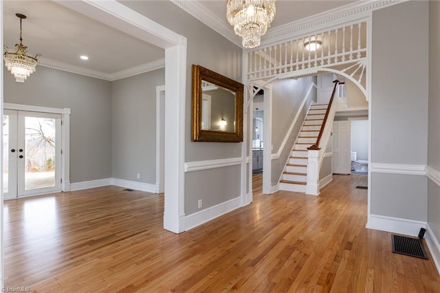 foyer entrance with crown molding, light hardwood / wood-style flooring, french doors, and a chandelier