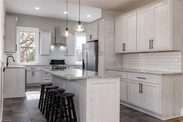 kitchen with wall chimney range hood, stainless steel appliances, a healthy amount of sunlight, and a kitchen island