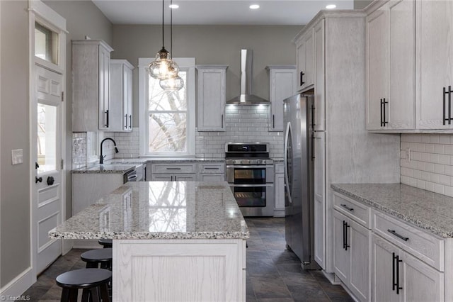 kitchen featuring wall chimney exhaust hood, appliances with stainless steel finishes, a kitchen island, pendant lighting, and white cabinets