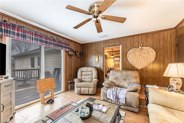 living room with ornamental molding, light hardwood / wood-style floors, ceiling fan, and wooden walls