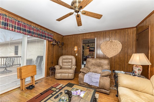 living room with wood walls, ceiling fan, light hardwood / wood-style floors, and ornamental molding