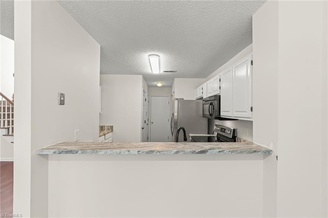 kitchen featuring white cabinets, a textured ceiling, kitchen peninsula, light stone countertops, and appliances with stainless steel finishes