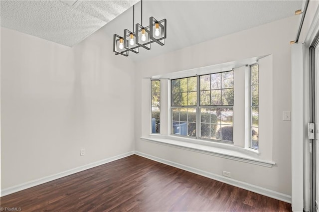 unfurnished dining area with a textured ceiling, a chandelier, a wealth of natural light, and dark hardwood / wood-style floors