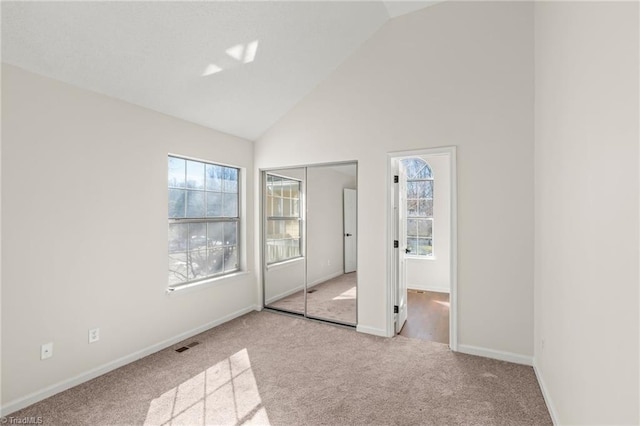 unfurnished bedroom featuring high vaulted ceiling, a closet, and light carpet