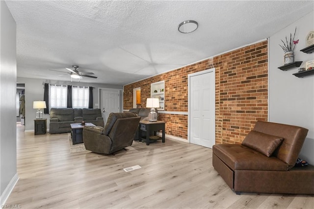 living room with light wood-style floors, a textured ceiling, a ceiling fan, and brick wall