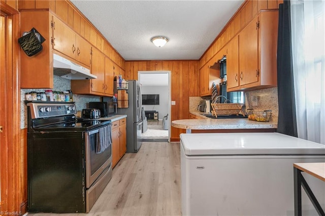 kitchen featuring appliances with stainless steel finishes, brown cabinets, light countertops, light wood finished floors, and under cabinet range hood