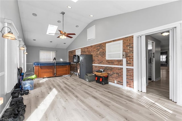 living room featuring wood finished floors, brick wall, recessed lighting, vaulted ceiling with skylight, and a ceiling fan