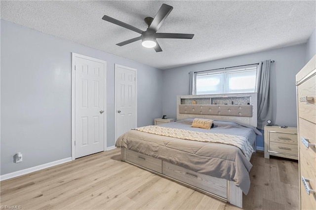 bedroom with a textured ceiling, multiple closets, a ceiling fan, baseboards, and wood finished floors