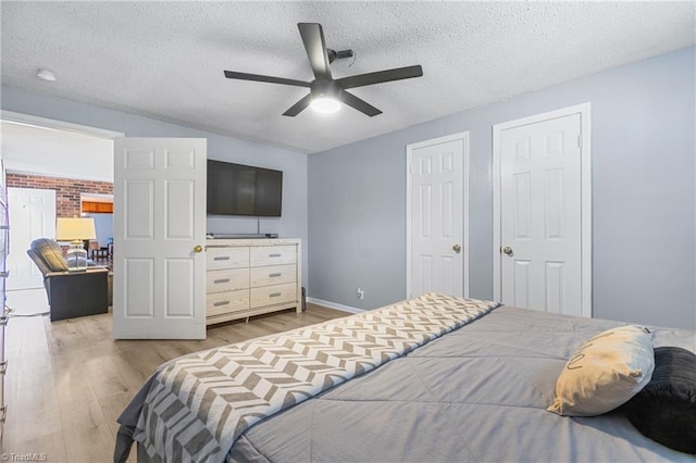 bedroom featuring a textured ceiling, multiple closets, a ceiling fan, baseboards, and wood finished floors