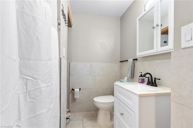 bathroom with vanity, toilet, tile walls, a textured ceiling, and tile patterned floors