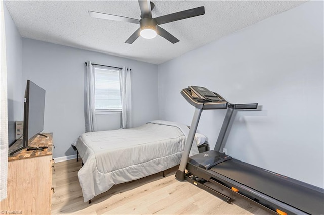 bedroom featuring light wood-type flooring, a ceiling fan, a textured ceiling, and baseboards