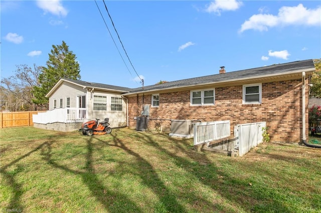 back of house featuring a chimney, central AC unit, brick siding, fence, and a yard