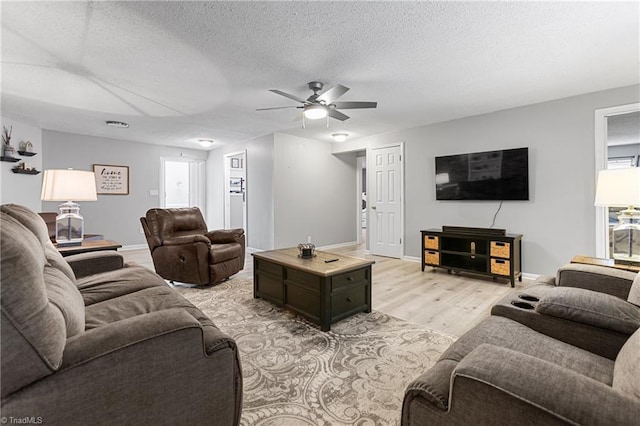 living room with light wood-style floors, baseboards, ceiling fan, and a textured ceiling