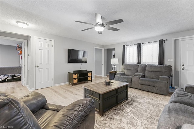 living room with baseboards, light wood-style flooring, a textured ceiling, and ceiling fan