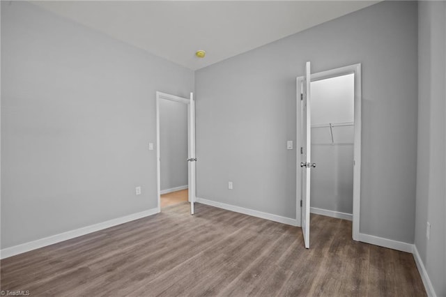 unfurnished bedroom with a closet, baseboards, wood finished floors, and a spacious closet