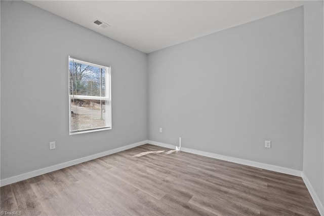 empty room with wood finished floors, visible vents, and baseboards