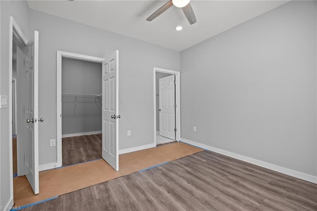 unfurnished bedroom with a spacious closet, a closet, baseboards, and a ceiling fan