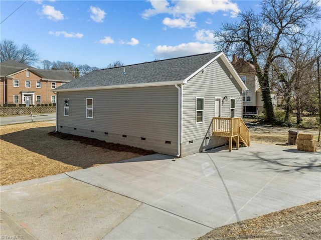 view of side of property featuring a shingled roof, a patio, and crawl space