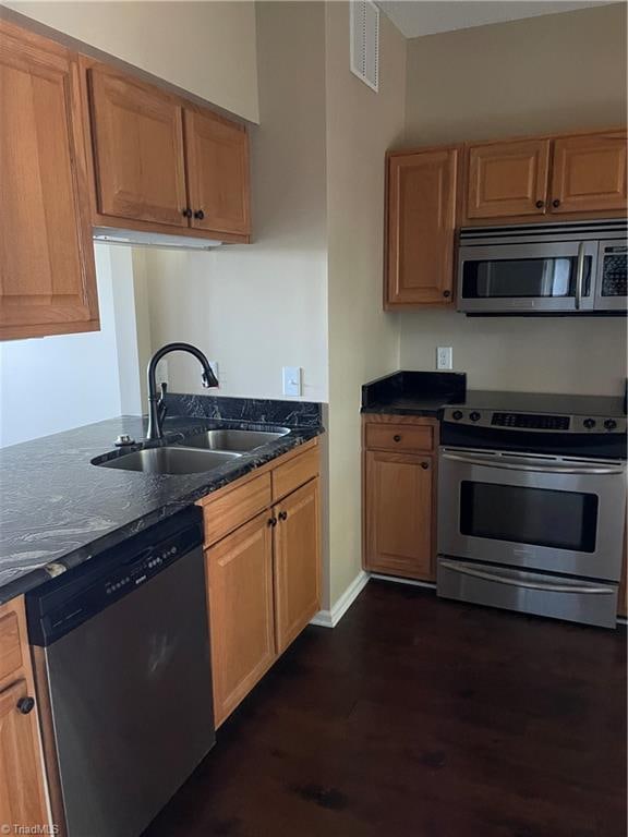 kitchen with dark stone countertops, stainless steel appliances, sink, and dark hardwood / wood-style floors