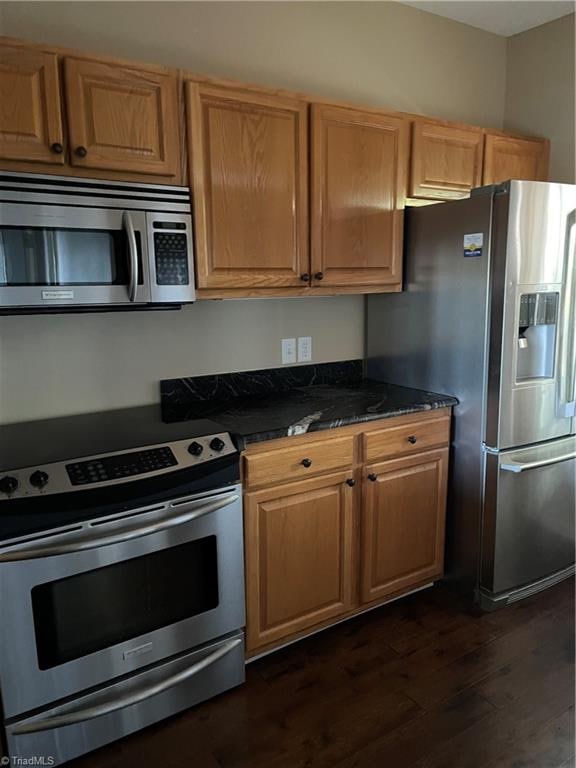 kitchen featuring dark stone countertops, stainless steel appliances, and dark hardwood / wood-style floors